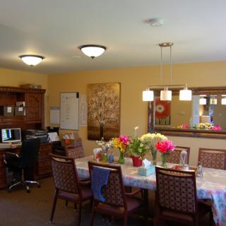 A cozy dining room with a table set, flowers, and a nearby computer desk.