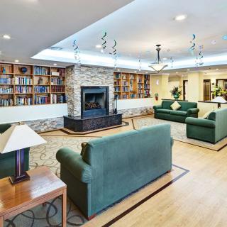 A cozy living room with a fireplace and bookshelves, featuring comfortable sofas and elegant chandeliers.