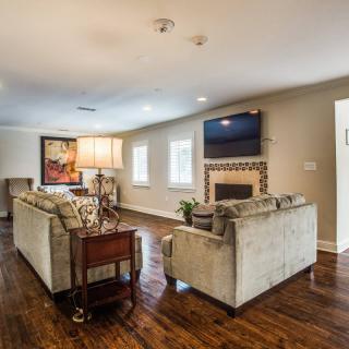 A spacious and well-lit living room featuring a cozy sofa, a modern fireplace with a television above it, and elegant hardwood floors.