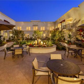 A beautifully lit courtyard with outdoor seating and a central fountain under an evening sky.