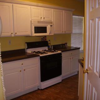 A small kitchen with white cabinets and a stove under a wall-mounted microwave.