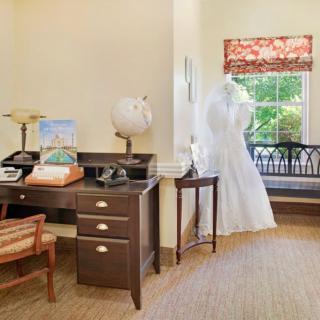 A vintage-style office with a desk featuring a typewriter, telephone, and globe, alongside a dress form by the window.