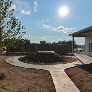 A sunny garden landscape featuring a circular concrete pathway and a raised platform.