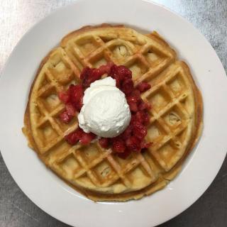 A delicious waffle topped with strawberries and whipped cream.