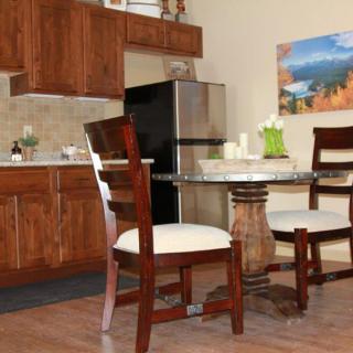 A modern kitchen with wooden cabinetry and a dining area featuring a round glass table and cushioned chairs.