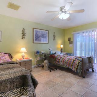 A cozy bedroom featuring twin beds with quilts, illuminated by a fan light and table lamps, with a sliding glass door providing natural light.