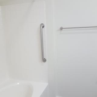 A minimalist bathroom with a bathtub, grab bar, and towel rack.