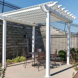 A white pergola provides shade over a patio set in a sunny garden area.