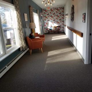 A brightly lit hallway featuring a cozy seating area with an armchair and a lamp.