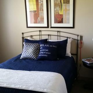 A neatly arranged bed with blue bedding and decorative pillows, adorned with artwork above.