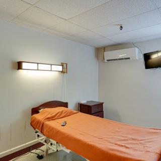 A clean and simple hospital patient room featuring an orange bedspread, air conditioning unit, and wall-mounted television.
