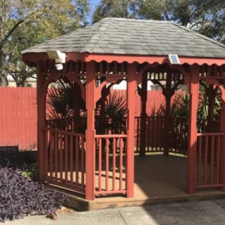 A wooden gazebo in a sunny garden setting.