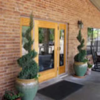 An entrance with a wooden door and decorative potted plants on a brick wall background.