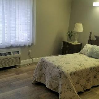 A cozy and simple bedroom featuring a bed, lamp, and natural light from the window.