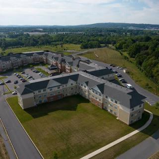 Aerial view of a large residential building complex surrounded by greenery and a parking area.