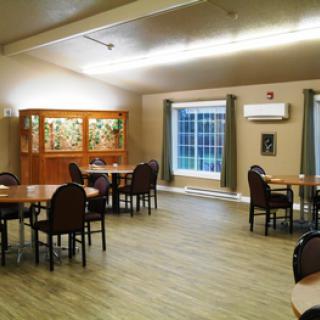 An empty dining room with tables and chairs, featuring a large window and wooden flooring.