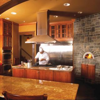 A chef cooking in a modern kitchen with wood cabinetry and a stone accent wall.