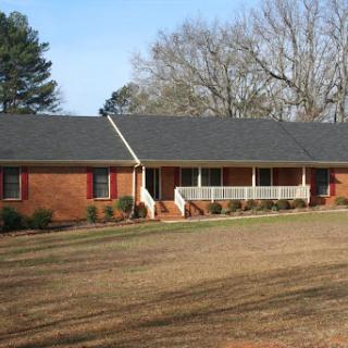 A charming brick ranch-style house surrounded by greenery and a clear blue sky.