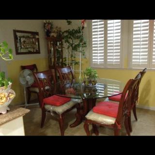 A cozy dining room with a glass table and wooden chairs, accented by indoor plants and artwork.