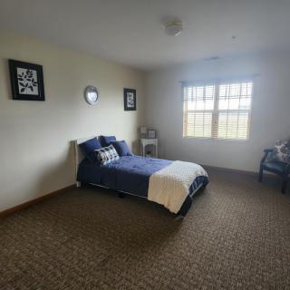 A minimalist bedroom with a bed by the window, featuring simple decor and carpeted flooring.