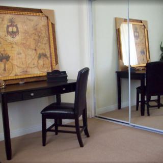 A room with a desk and chair facing a large mirrored closet, featuring a framed map on the wall.