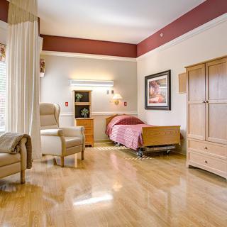 A well-lit hospital room featuring a bed, chairs, and wooden furniture with a polished floor.