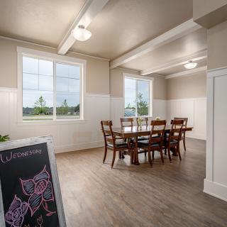 A bright dining room with a wooden table and chairs, featuring large windows and wooden flooring.