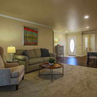 A cozy living room with a sofa, armchair, and coffee table, adjacent to a dining area.