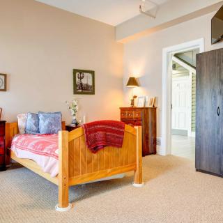 A cozy bedroom with a wooden bed, decorated with a red blanket and pillows, featuring a dresser and wall art.