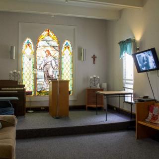 A small chapel interior with stained glass windows, a pulpit, and a pew.