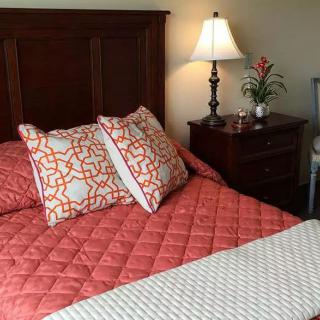 A cozy bedroom with a quilted bedspread and decorative pillows next to a nightstand with a lamp.