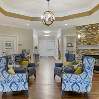 A modern and cozy living room with patterned armchairs arranged around a coffee table, featuring wood flooring and a stylish chandelier.