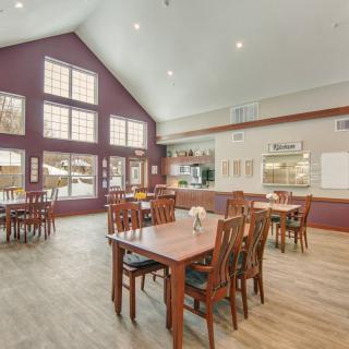 A spacious dining area with wooden tables and chairs, featuring large windows and bright lighting.