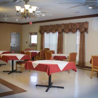 An empty dining room with tables covered in red and white tablecloths, wooden chairs, and decorative curtains.