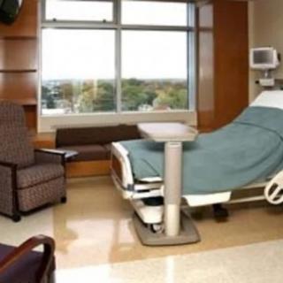 A hospital room with a bed, medical equipment, and seating by a window.