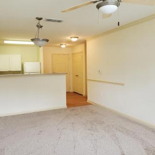 A spacious and well-lit apartment living area featuring a kitchen in the background.