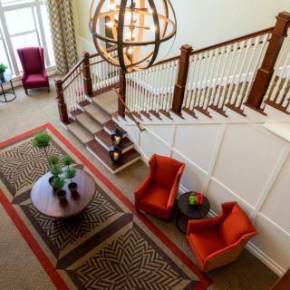 A stylish lobby features a staircase, vibrant chairs, and a decorative table under a large chandelier.