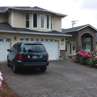A suburban house with a car parked in the driveway, featuring a two-car garage and flowering plants.