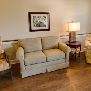 A cozy living room with a sofa, chairs, a lamp, and a painting on the wall.