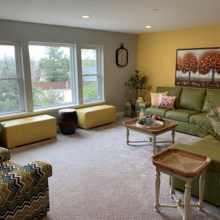 A colorful living room with green sofas, yellow ottomans, and large windows providing ample natural light.