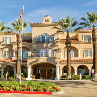 A large building with a grand entrance surrounded by palm trees and neatly arranged flower beds.