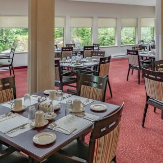 A spacious restaurant dining area with neatly arranged tables and chairs, featuring large windows for natural light.