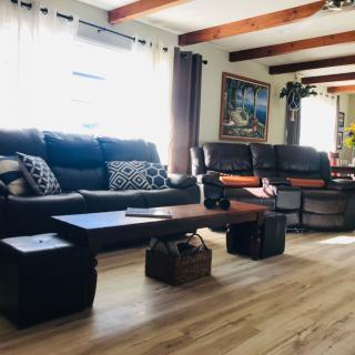 A cozy living room with sofas, a coffee table, and wooden floors, illuminated by natural light from the windows.