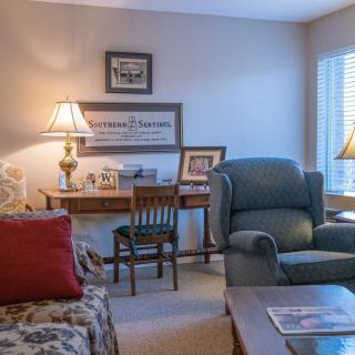A cozy living room with a comfortable armchair and a small desk with lamps providing warm lighting.