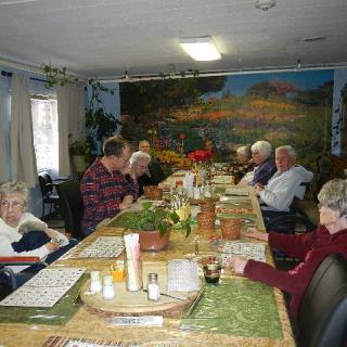 A group of seniors gathered around a dining table indoors, sharing a meal together.