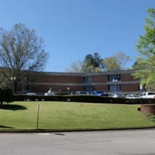 A brick building with cars parked in front, surrounded by grass and trees under a clear blue sky.