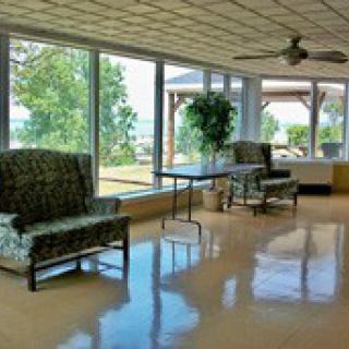 A bright lounge area with large windows showcasing a scenic outdoor view, furnished with comfortable chairs and greenery.