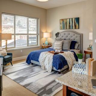 A cozy bedroom with a neatly made bed featuring blue and white bedding, stylish decor, and natural light from a large window.