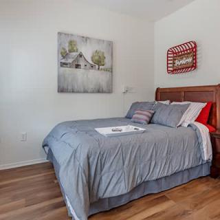 A cozy bedroom featuring a neatly made bed with gray bedding, artwork on the walls, and a wooden floor.