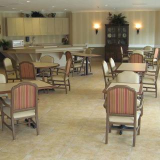 A spacious dining room with multiple tables and chairs, featuring a kitchen area in the background.